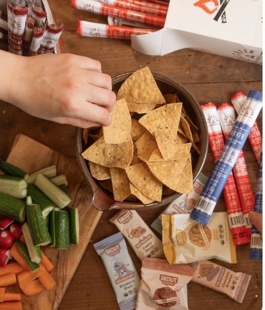Hands reaching for snacks and fresh vegetables on a wooden table